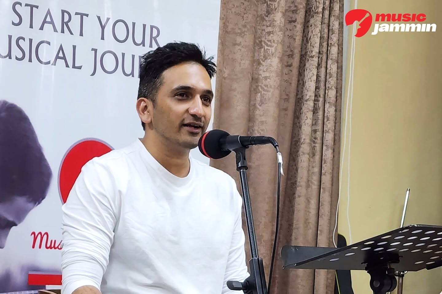 Host speaking on mic beside a Start Your Musical Journey banner